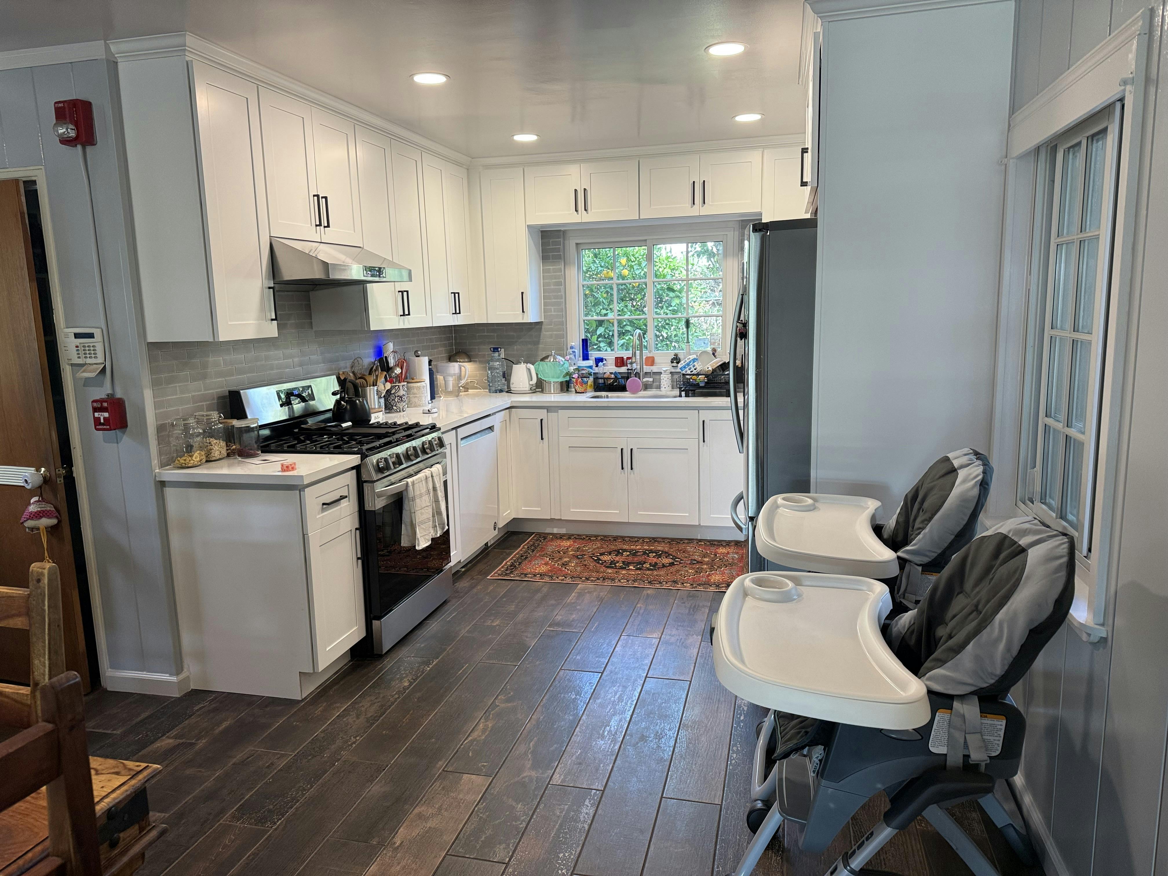 Kitchen with white cabinets, dark wood floors, and two baby high chairs