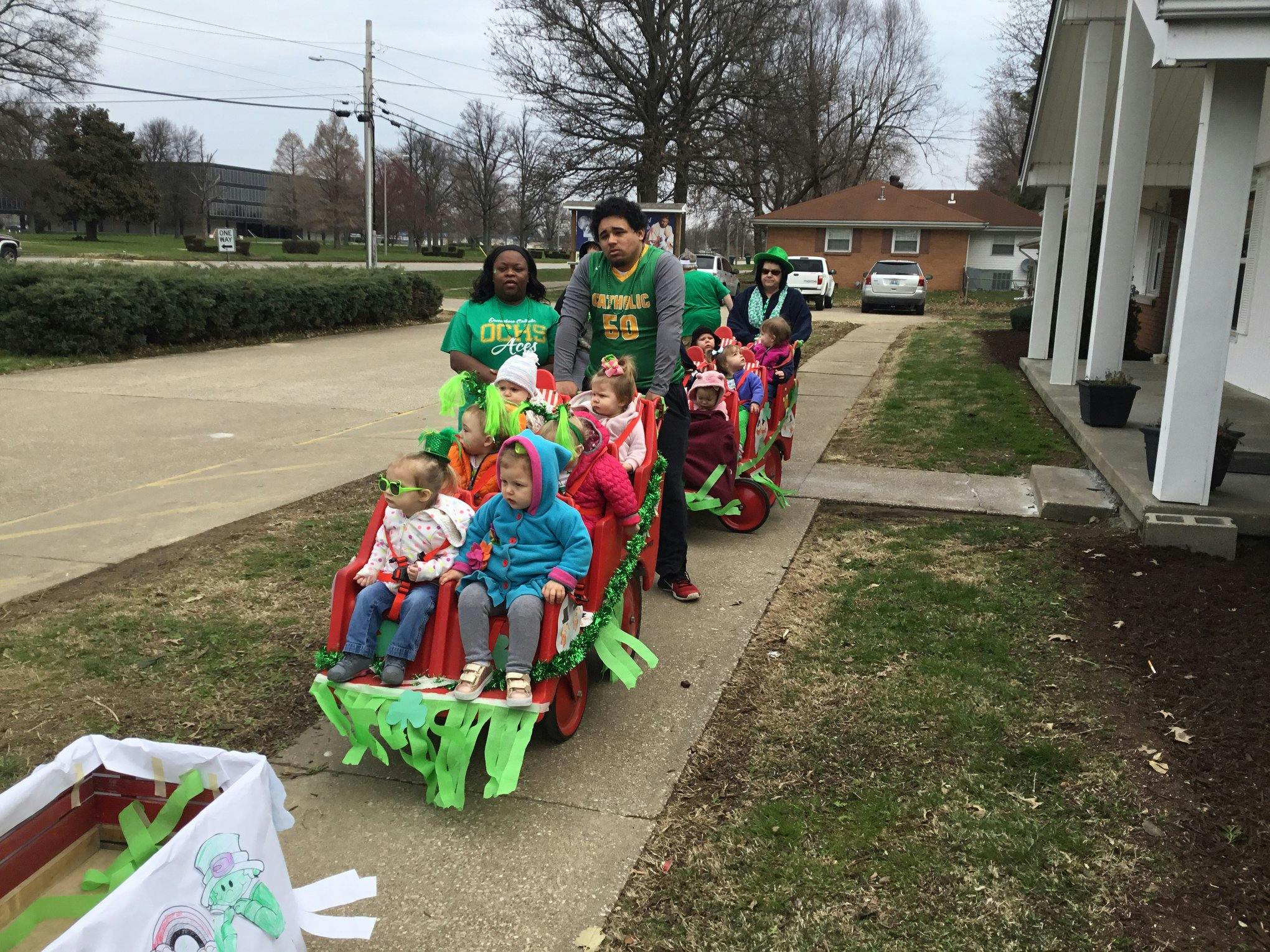 Adults pulling children in decorated wagons on a sidewalk
