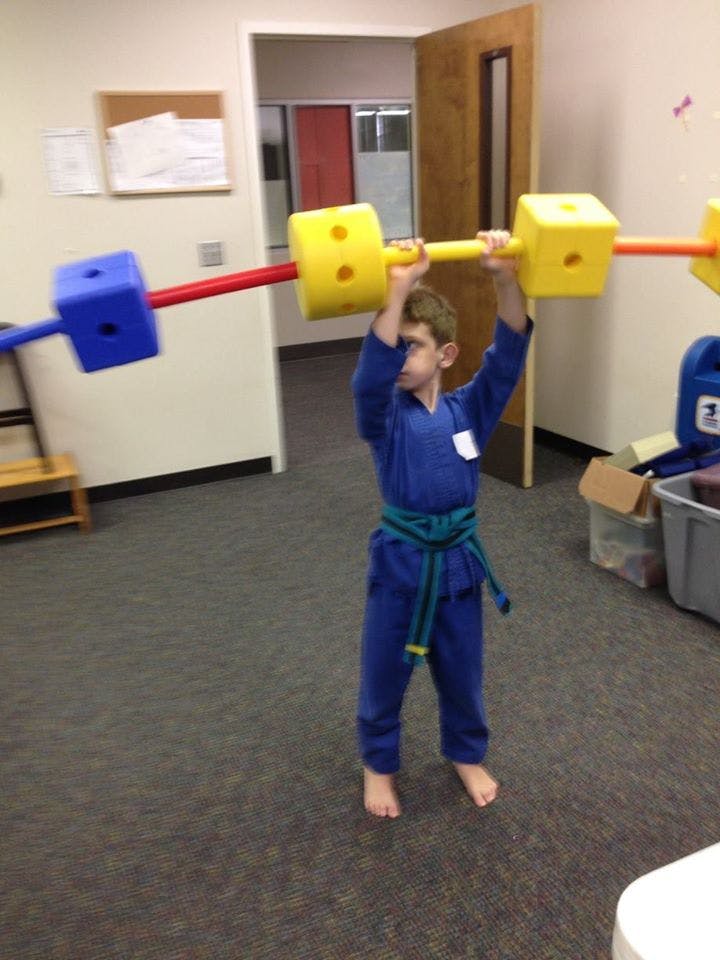 Child in blue uniform holding a toy barbell overhead