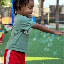 Child reaching for bubbles outdoors