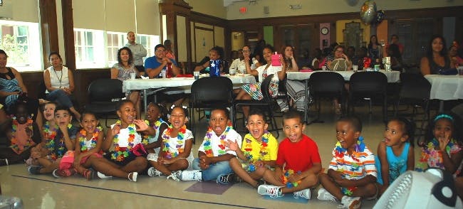 Children sitting on the floor in front of adults at tables
