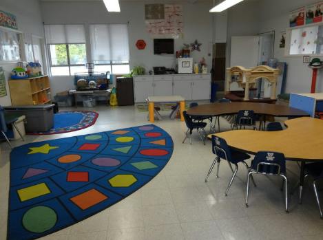 Classroom with tables, chairs, and a colorful rug with shapes