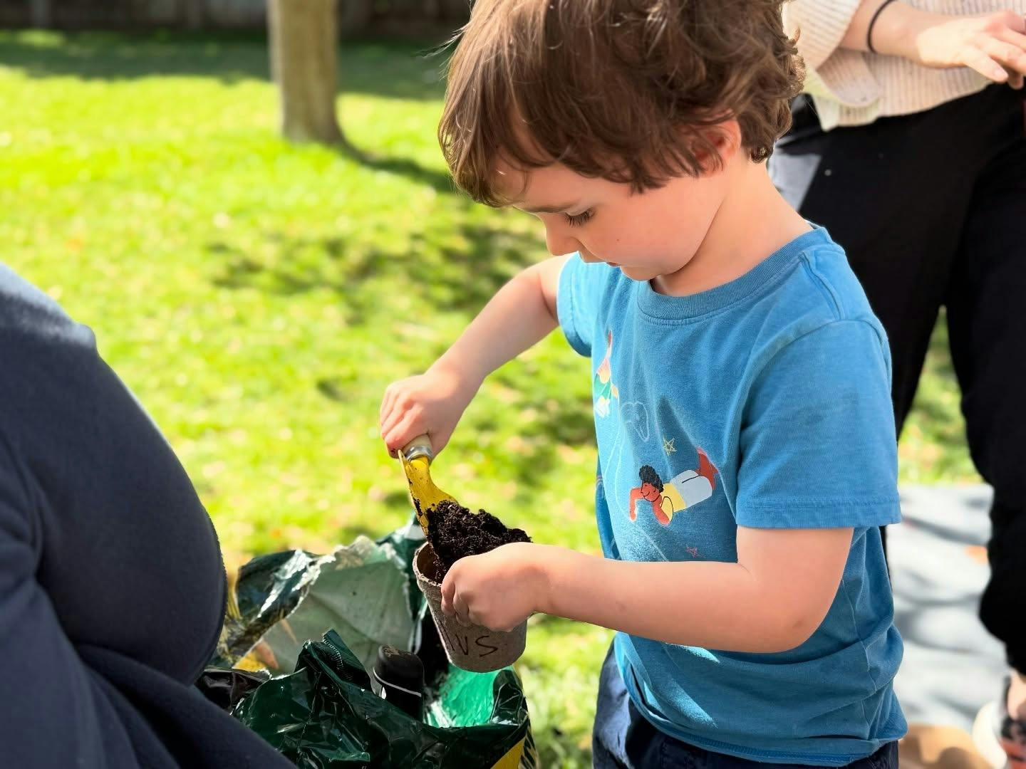 Child filling a small pot with soil using a hand shovel