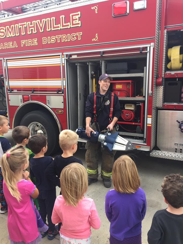 Firefighter holding equipment for a group of children in front of a fire truck