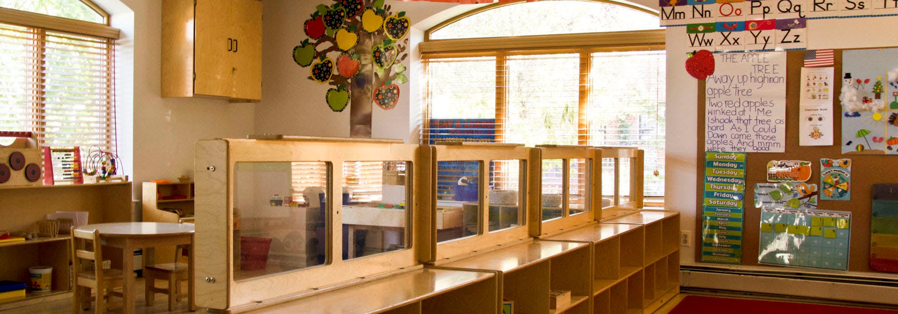 Classroom with wooden furniture, blinds on windows, and learning decorations