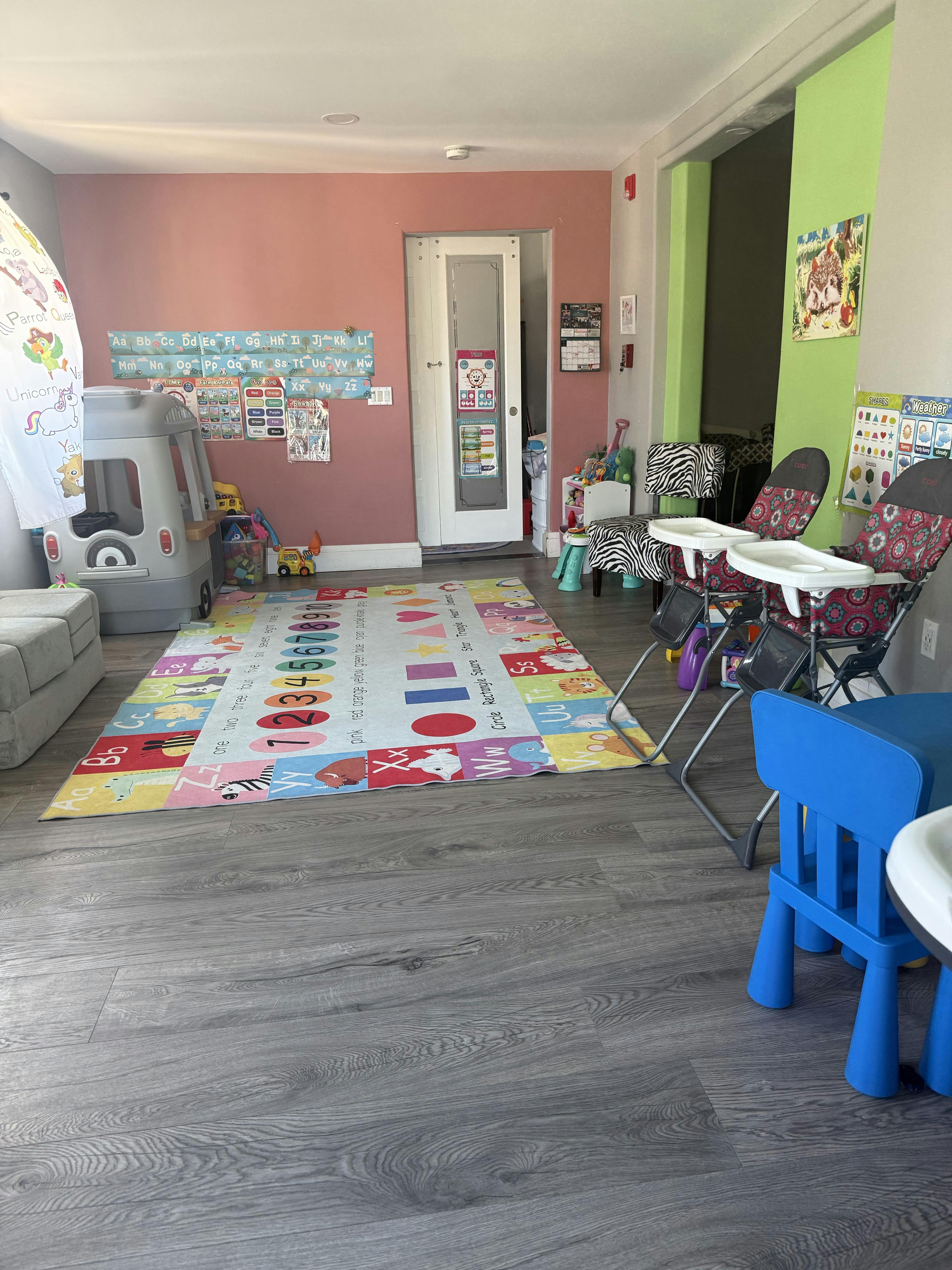 A colorful playroom with an ABC rug, toddler toys, high chairs, and charts