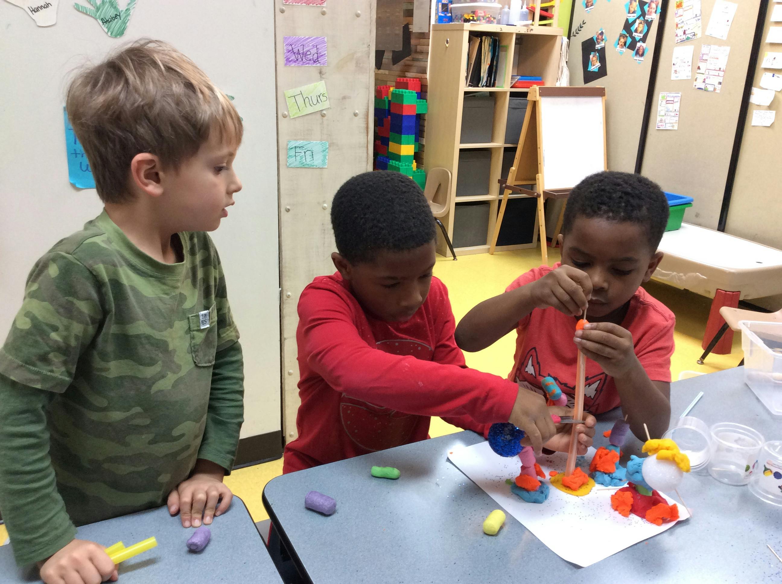 Three children playing with colorful building toys at a table in a classroom