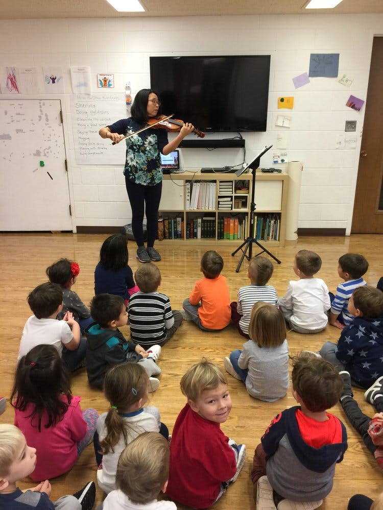 Person playing violin for a group of children sitting on the floor