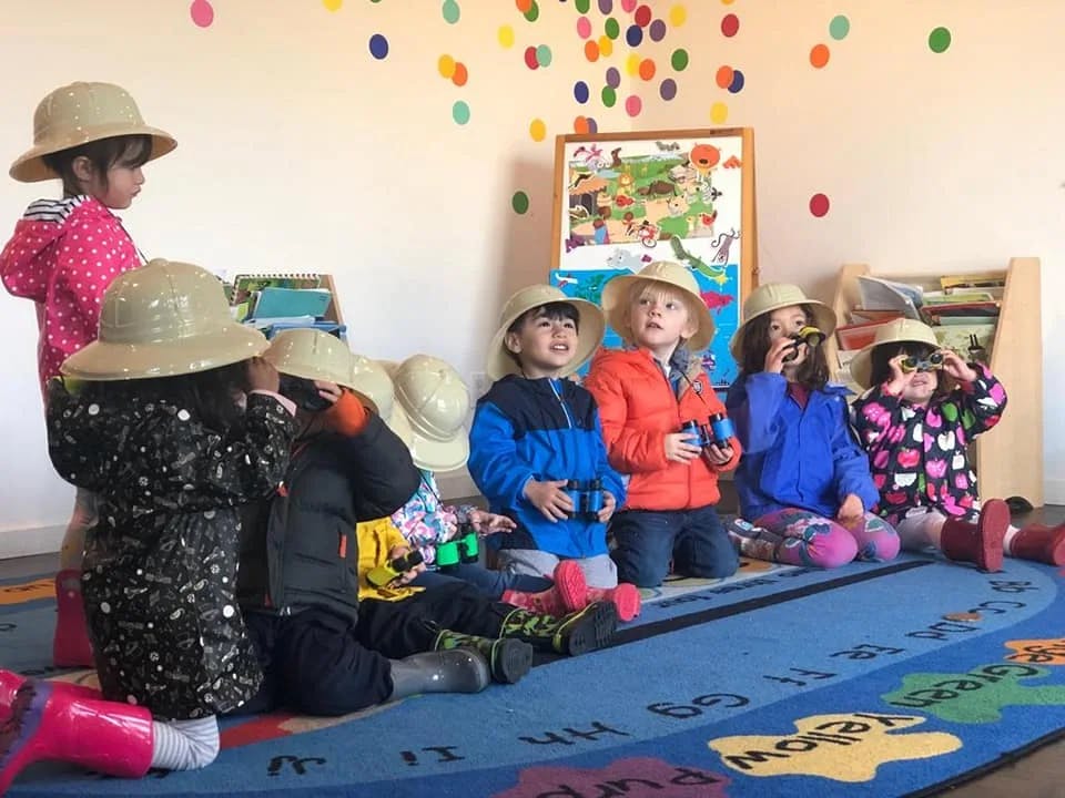 Children in safari hats playing with binoculars in a classroom