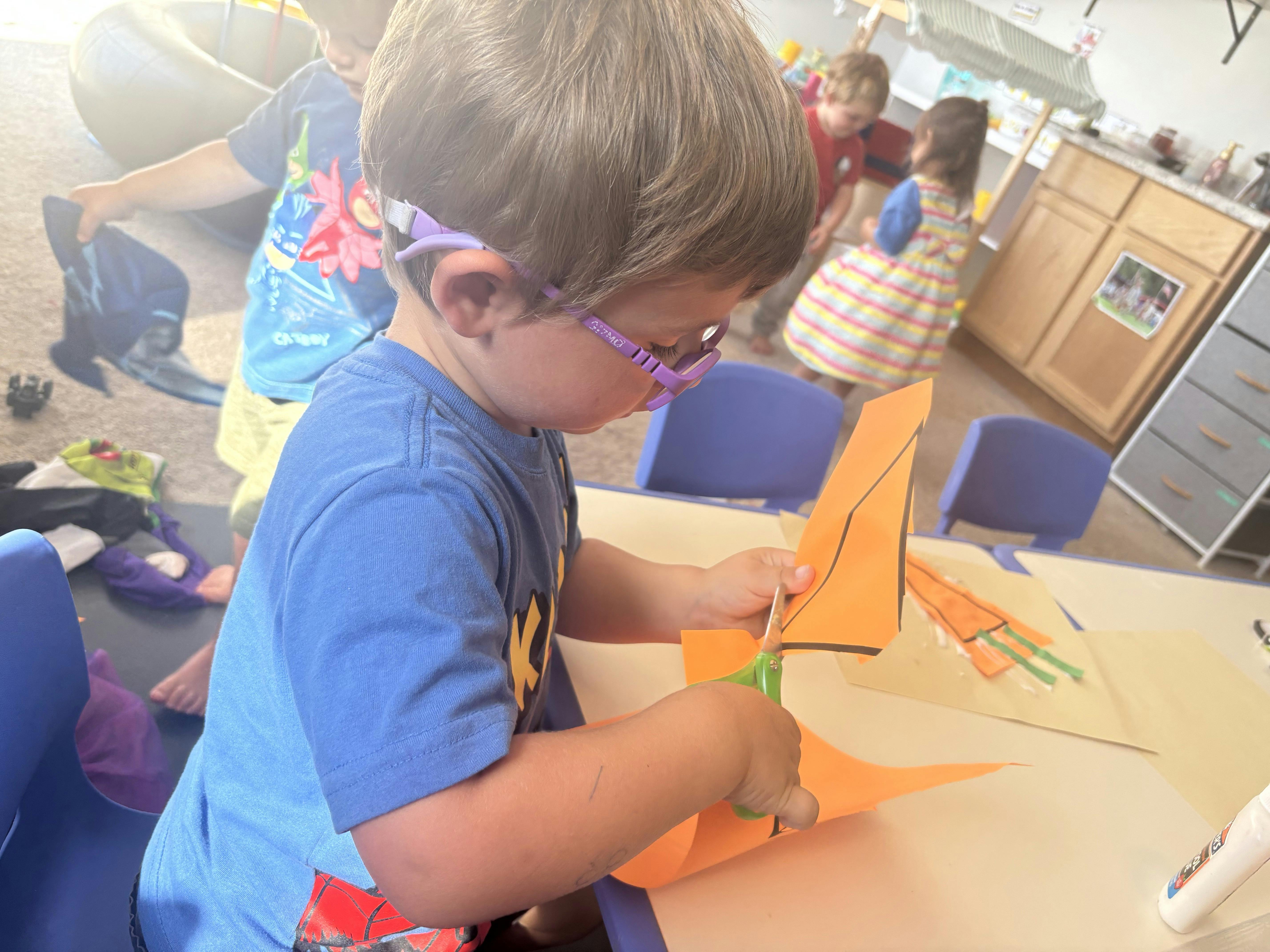 Child with glasses cutting orange paper with scissors