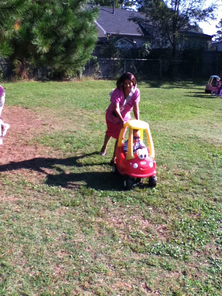 Person pushing a child in a red toy car on grass