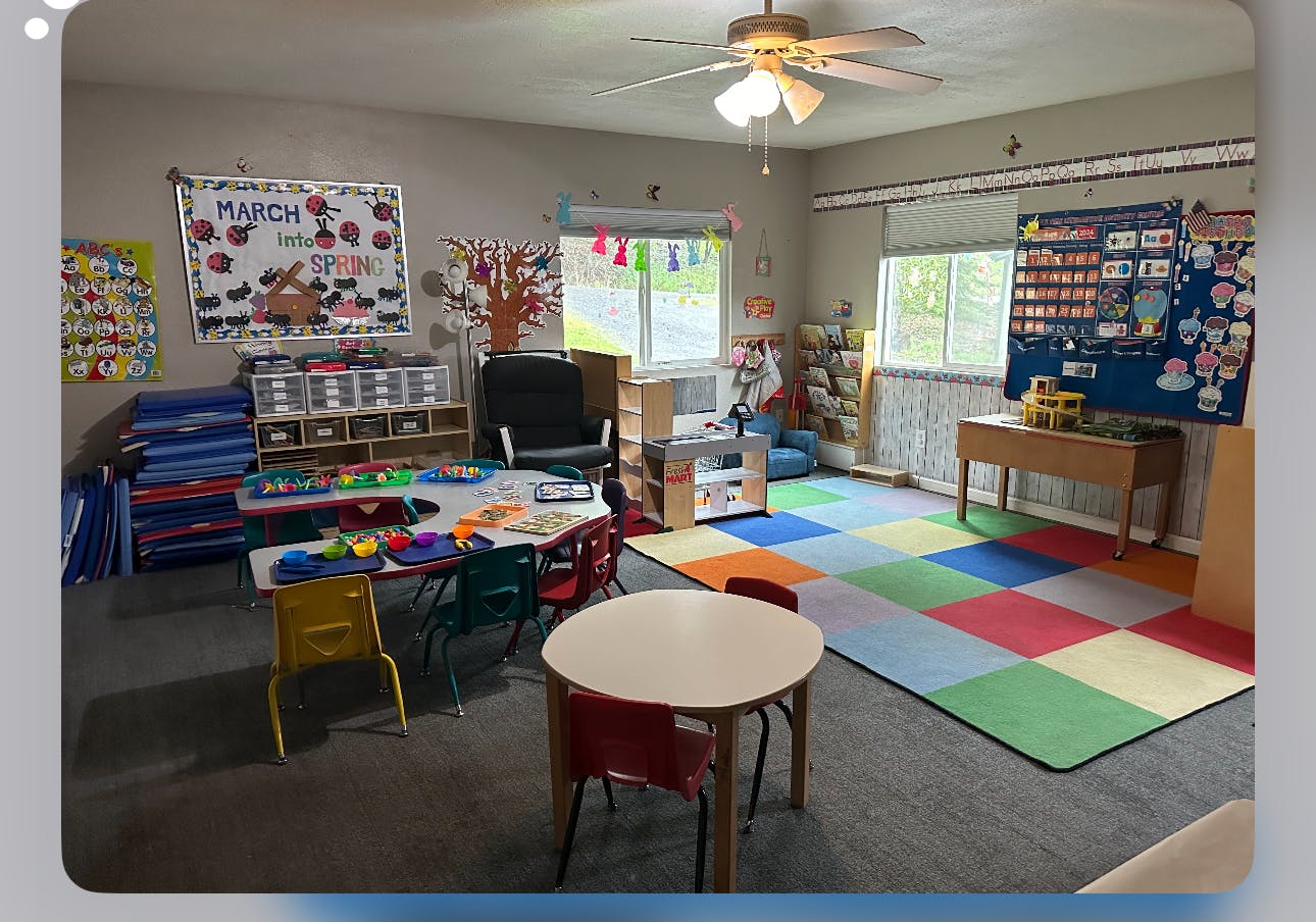 Classroom with small tables and chairs, colorful rug, and educational posters