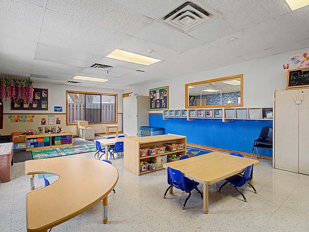 Classroom with child-sized tables and chairs, storage, and a blue wall