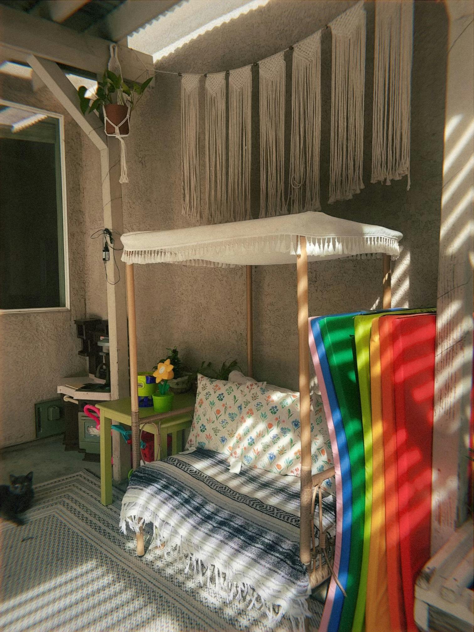 Small canopy bed with floral pillows and a blanket on a sunlit patio