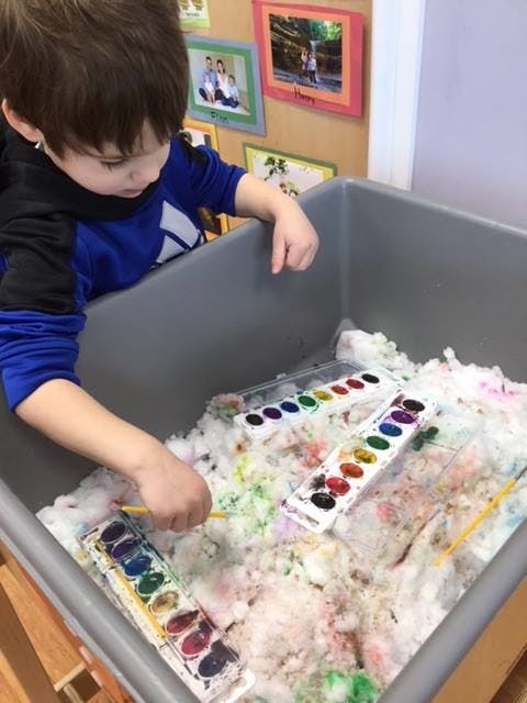 Child painting with watercolors in a bin of white material