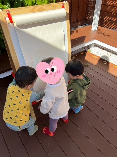 Three children standing around an easel with a roll of paper