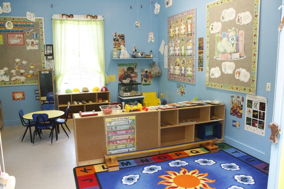 Classroom with small tables and chairs, shelves, and colorful rug