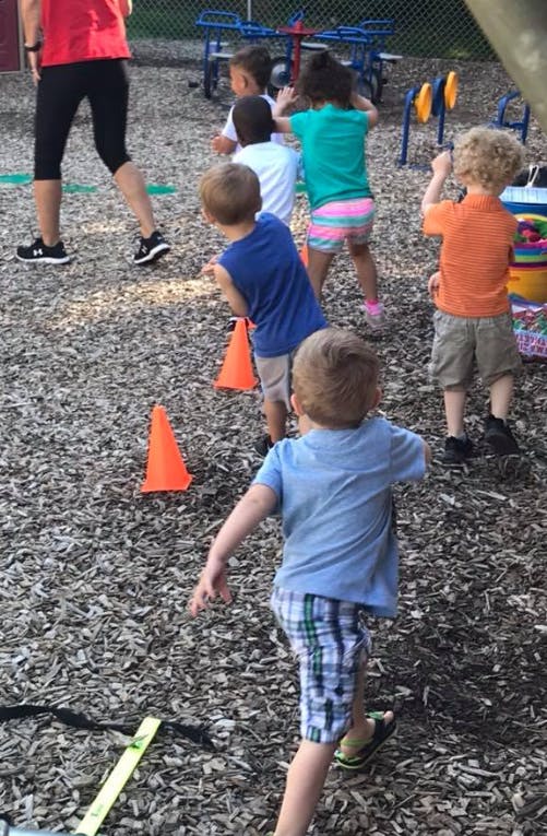 Children playing outdoors with orange cones and an adult