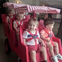 Multiple children in a red multi-seat stroller with striped canopies