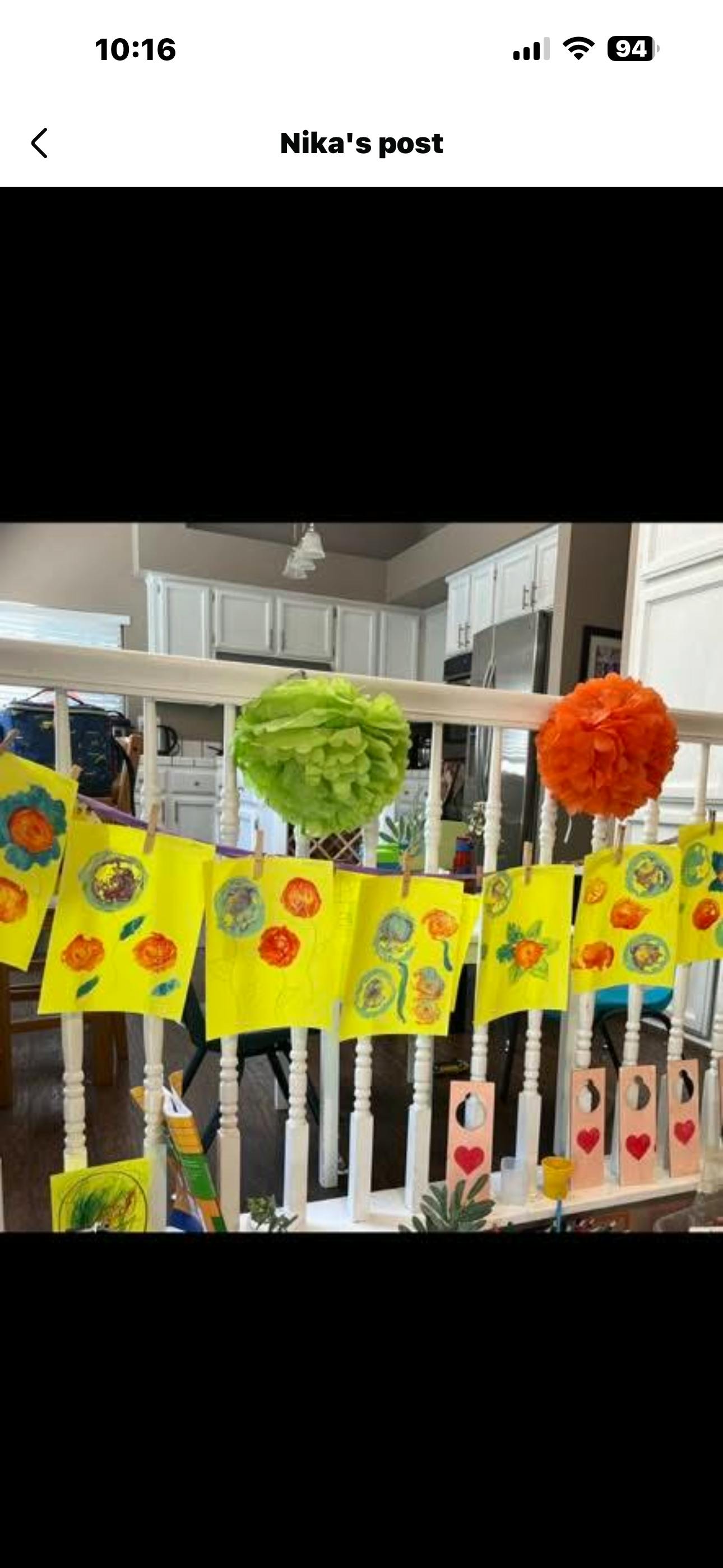 Child artwork hung on a staircase railing with paper pom-poms
