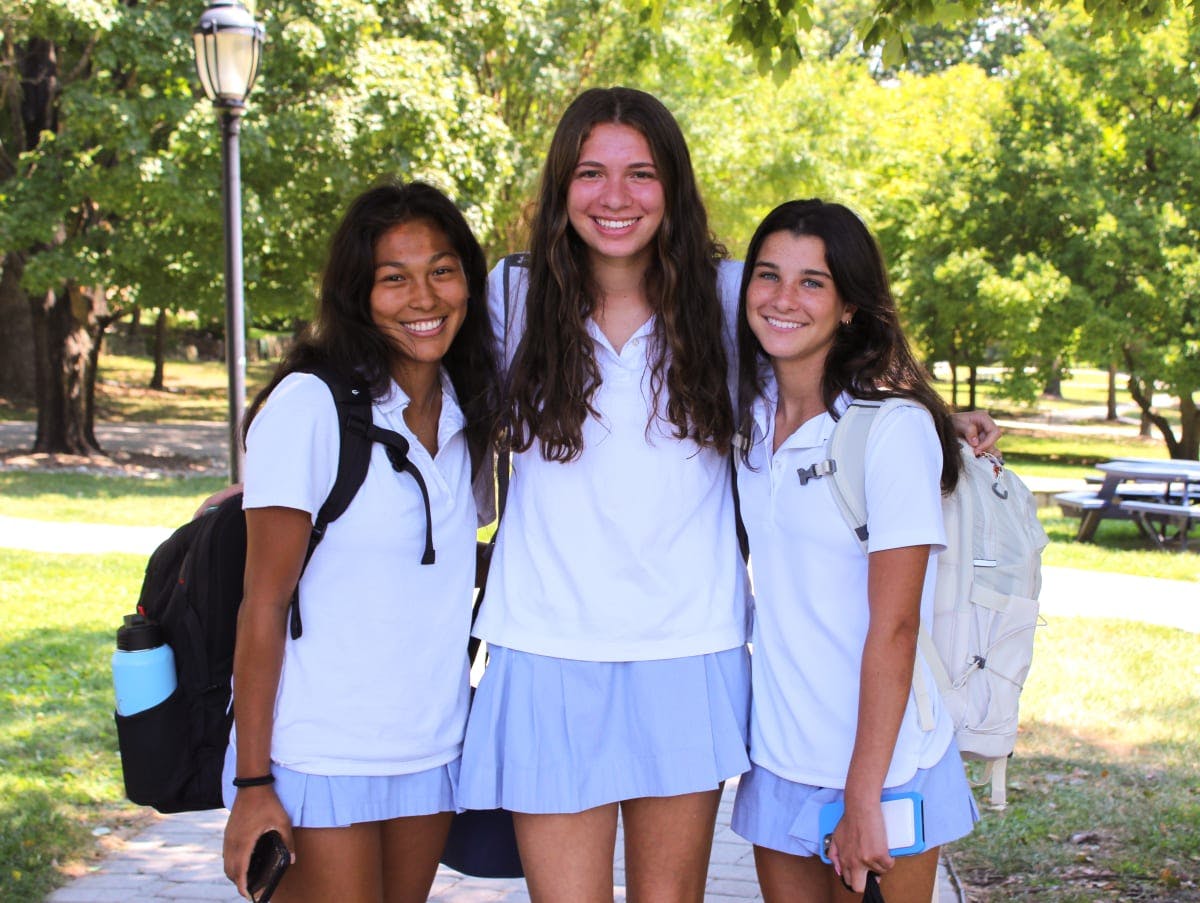 Three teens in white shirts and light blue skirts standing outdoors
