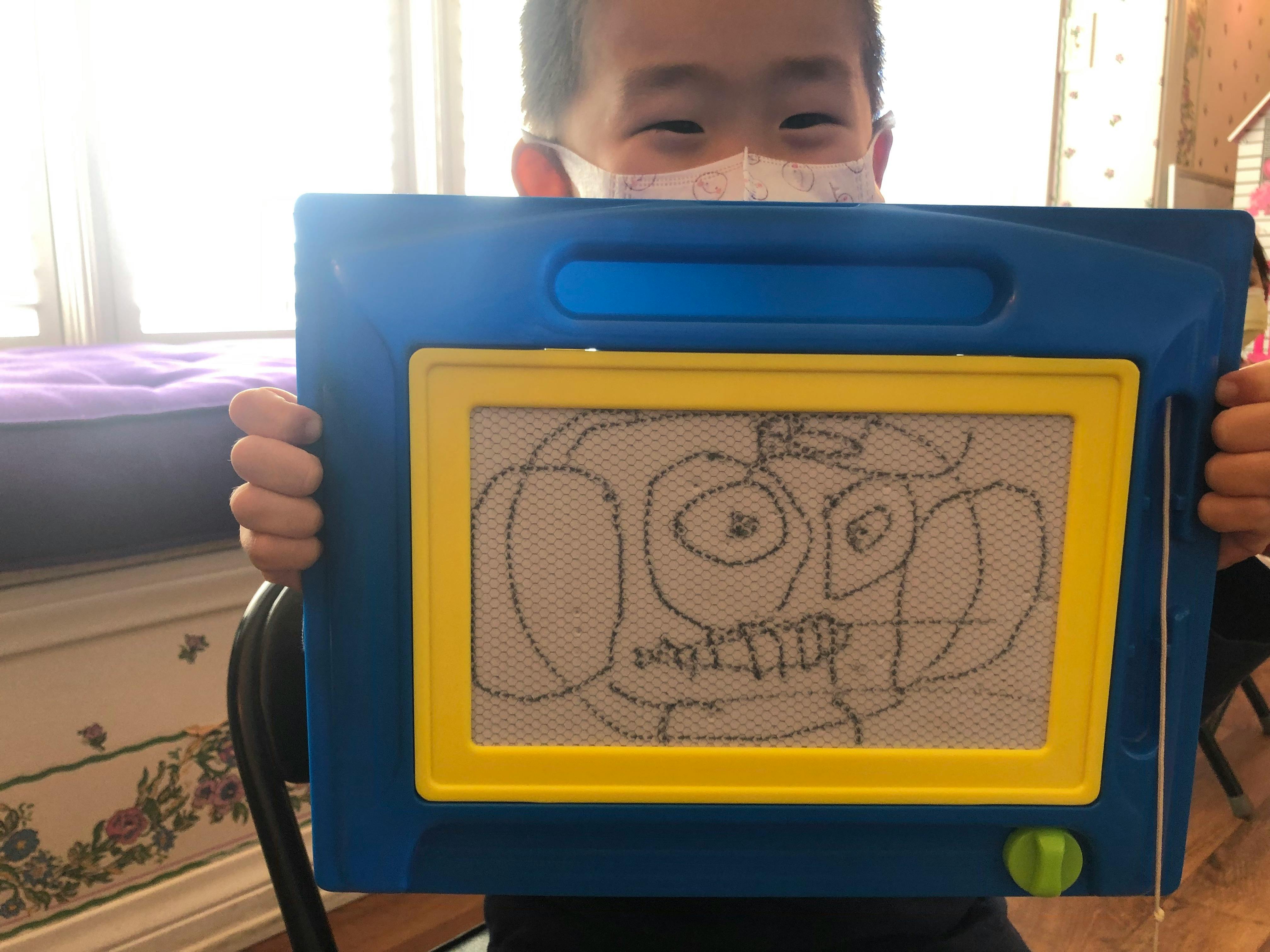 Child holding up a blue drawing board with a doodle on it