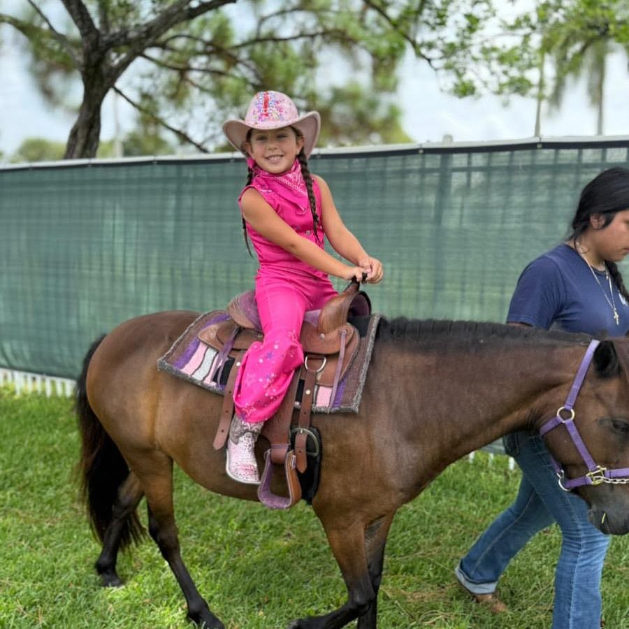 Child in a pink cowboy outfit riding a pony