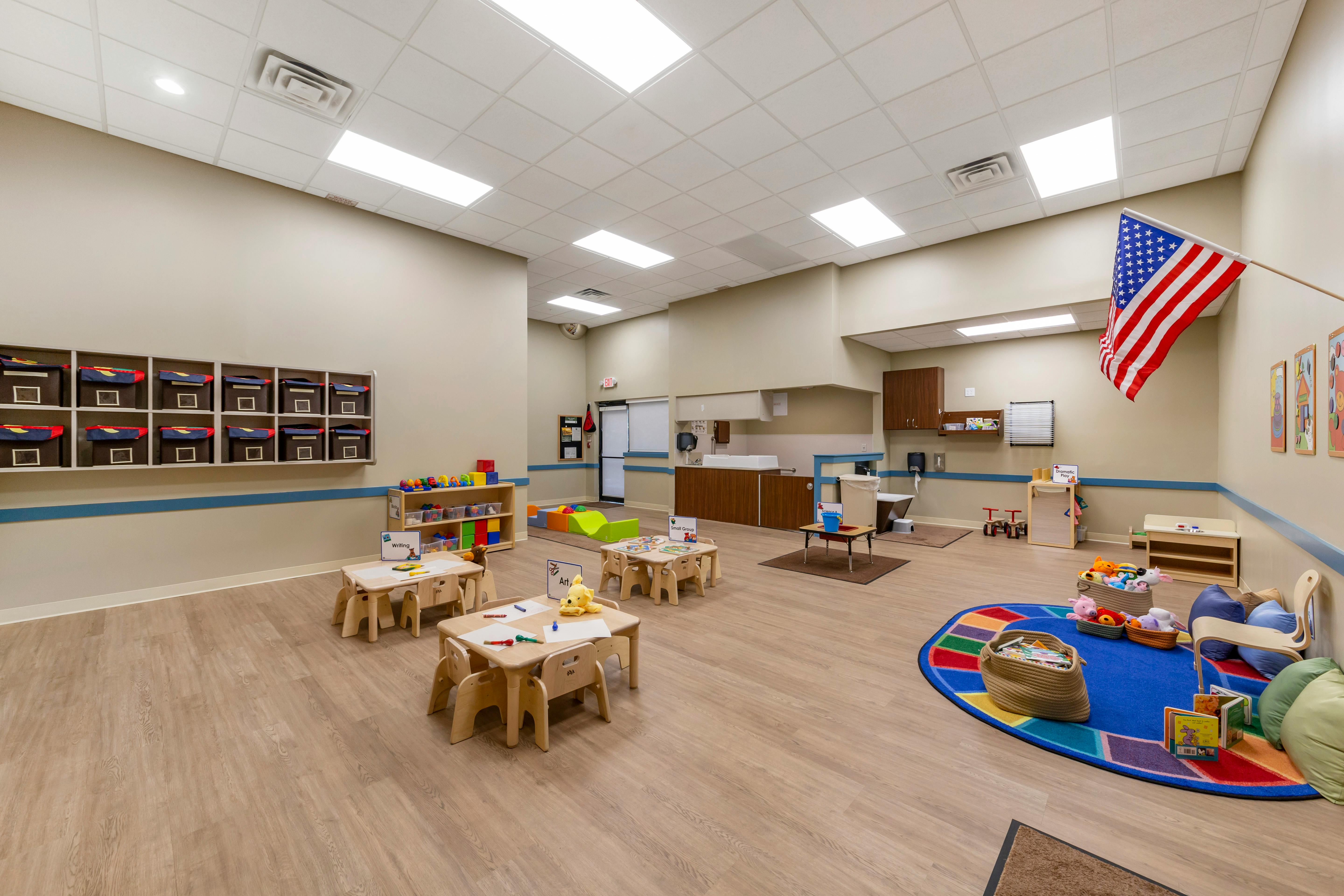 Classroom with small tables, storage bins, a colorful rug, and a US flag