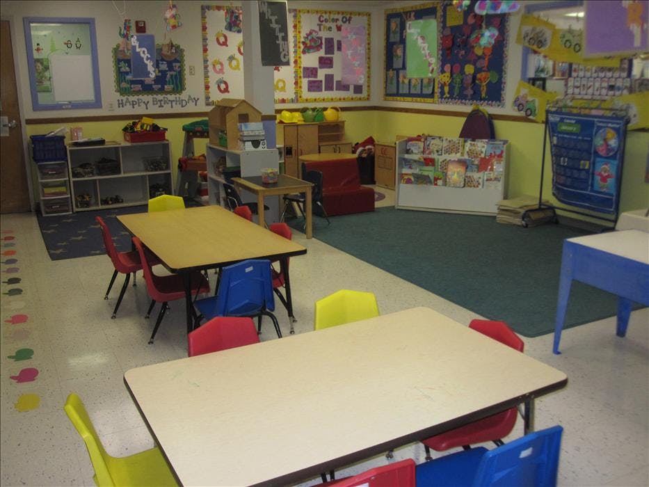 A classroom with small tables, colorful chairs, and educational posters on the walls