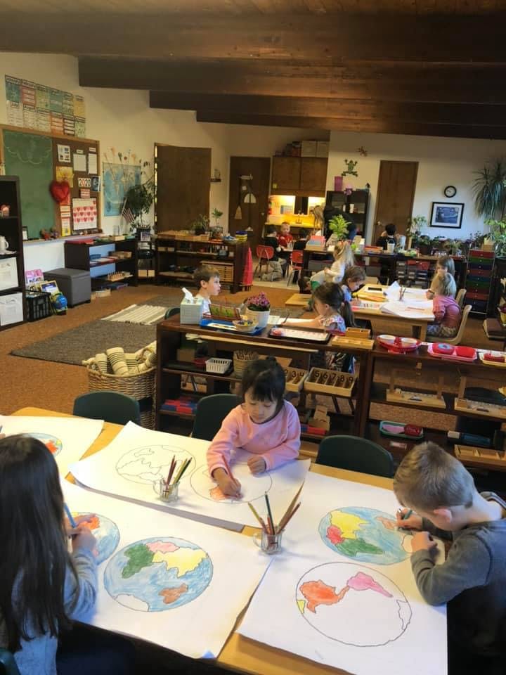 Children coloring world maps in a classroom