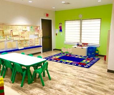 Classroom with small table and chairs, colorful rug, and artwork on wall