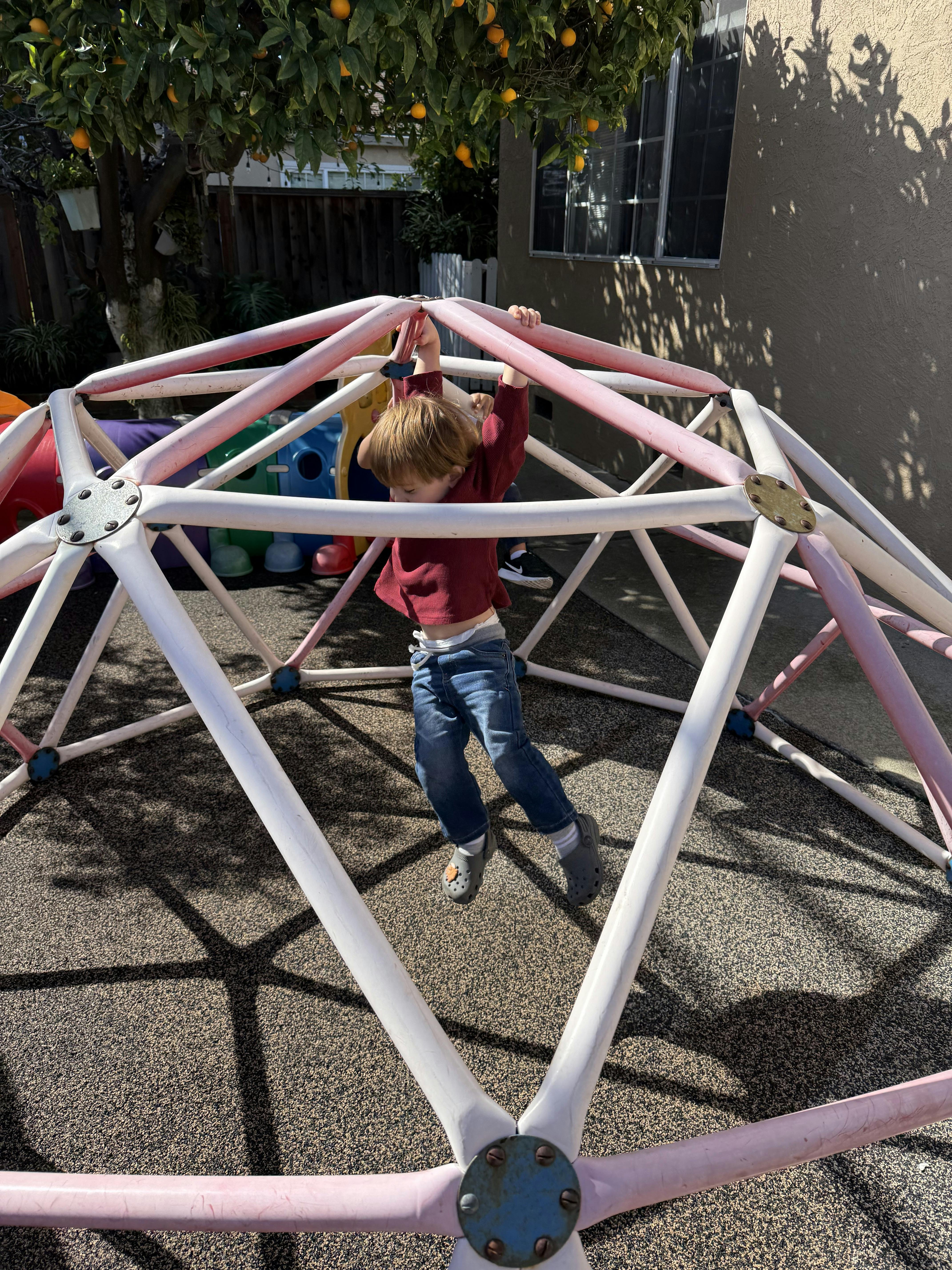 Child hanging from a pink and white geodesic dome climber