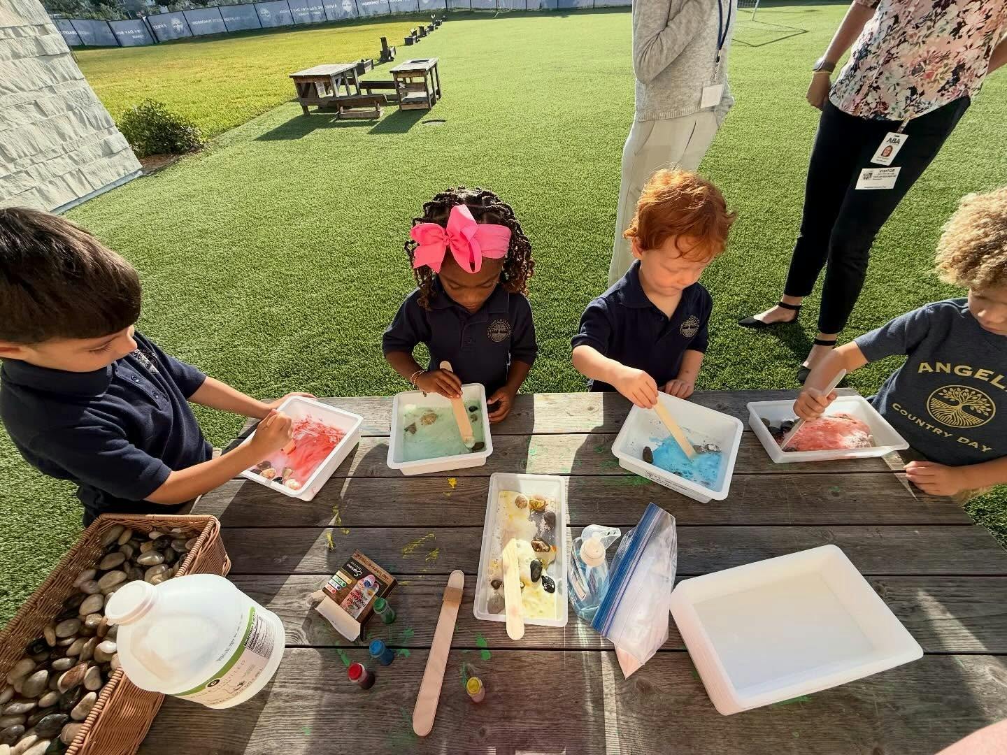 Children painting stones with wooden sticks at an outdoor table