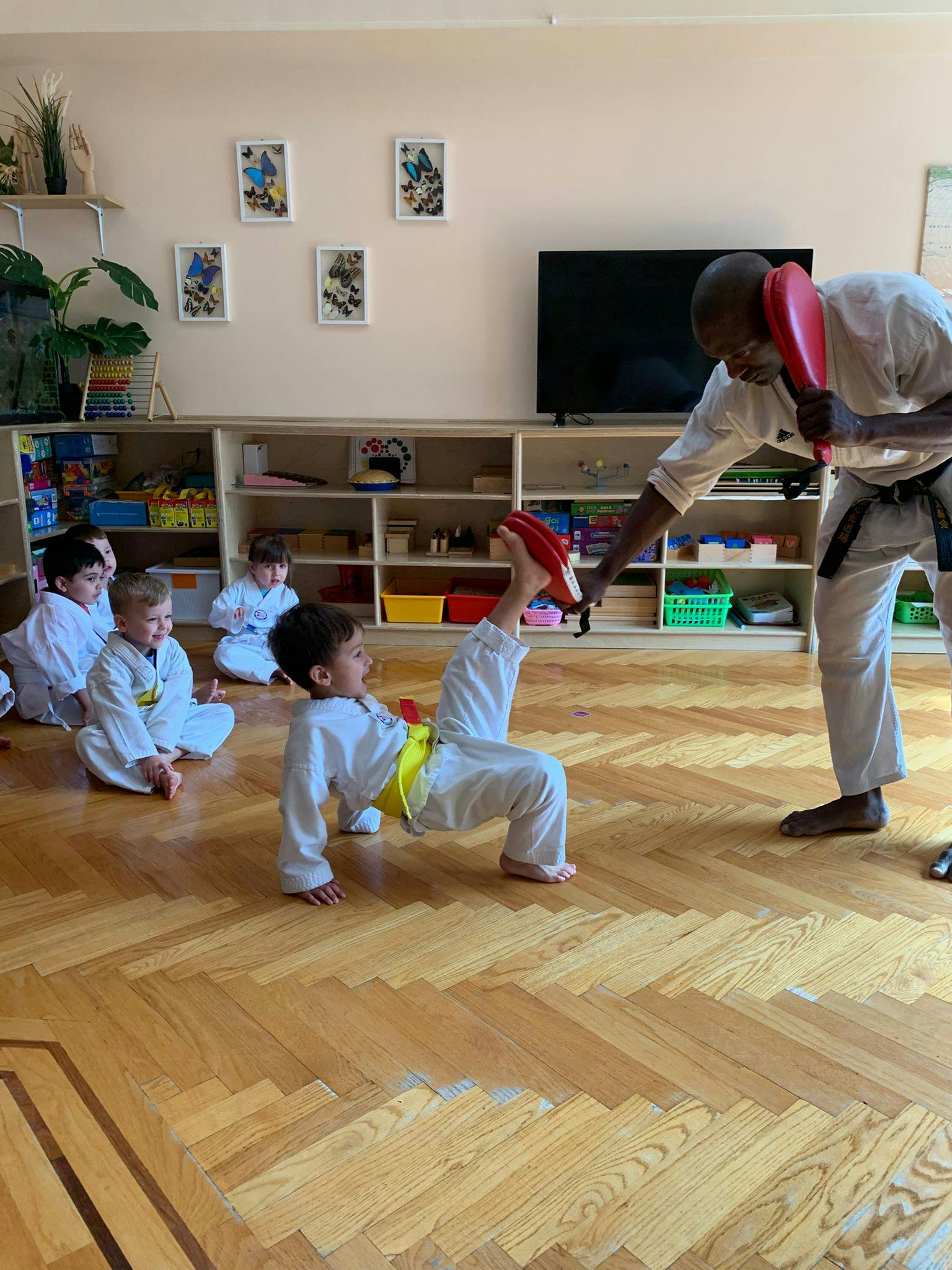 Adult and child in martial arts uniforms practicing a kick with a pad