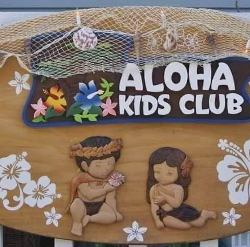 Aloha Kids Club sign with two carved figures and flowers