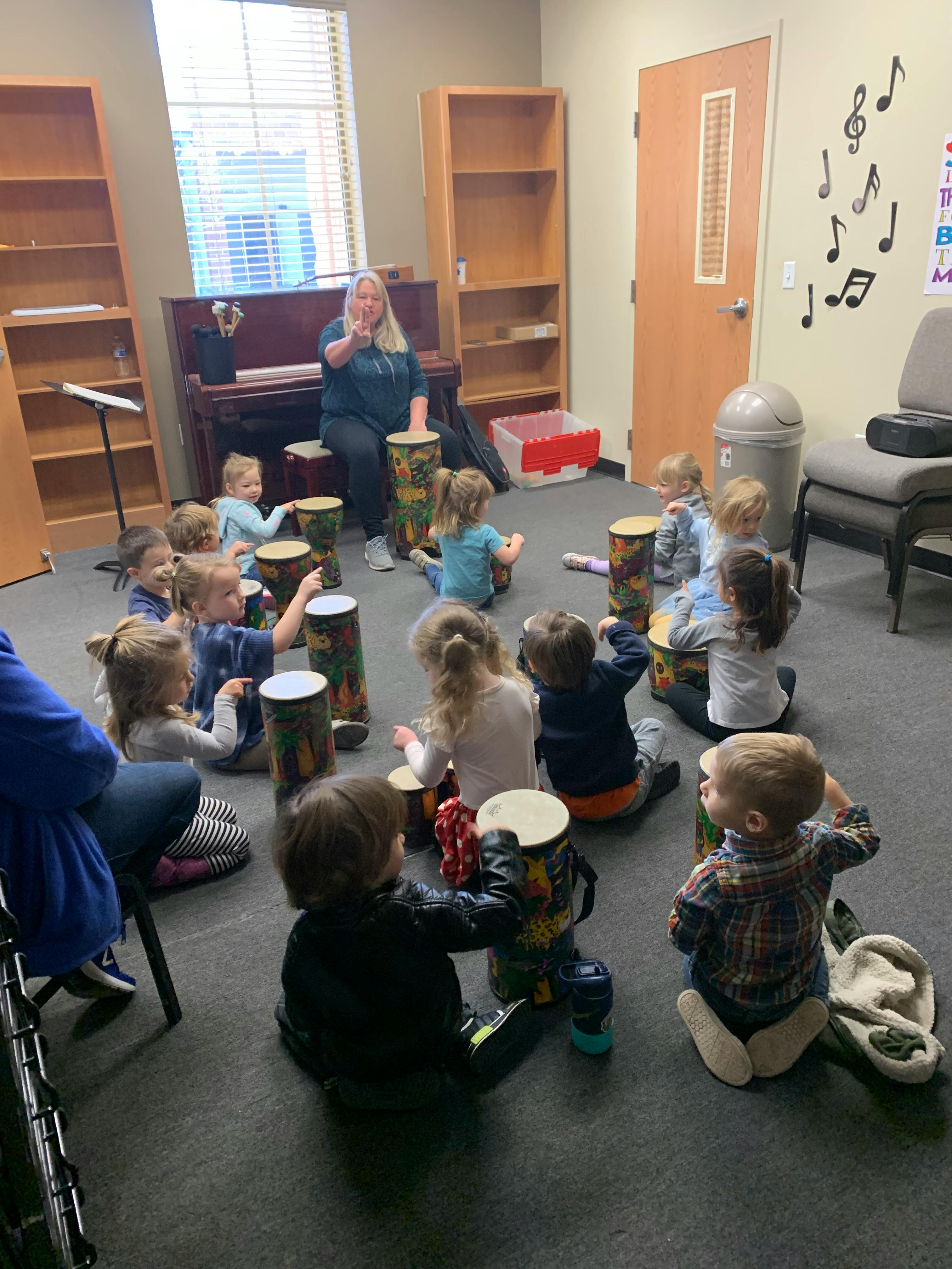 Person leading a group of children playing drums in a music class