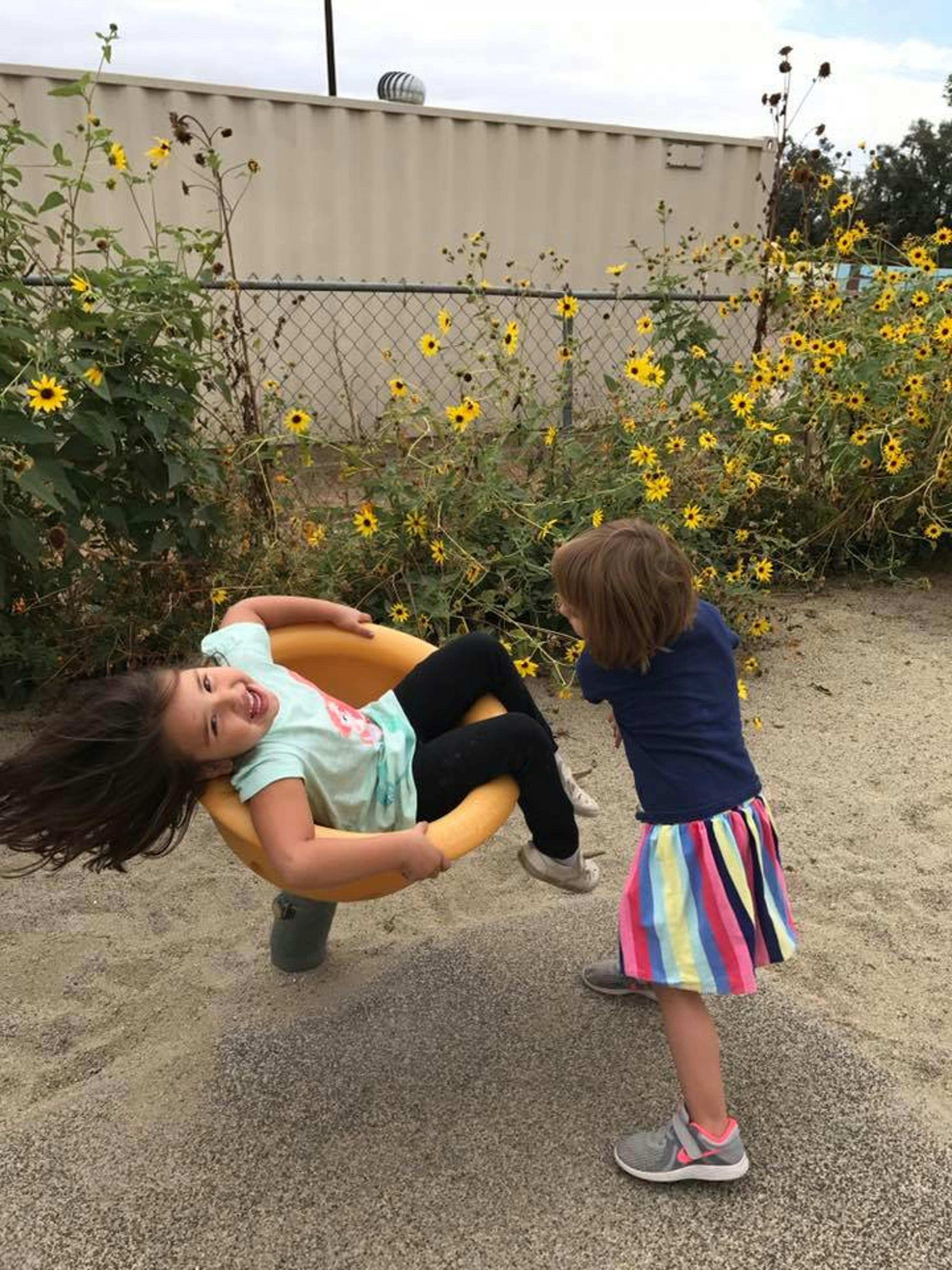 Child on a yellow playground spinner with another child standing nearby