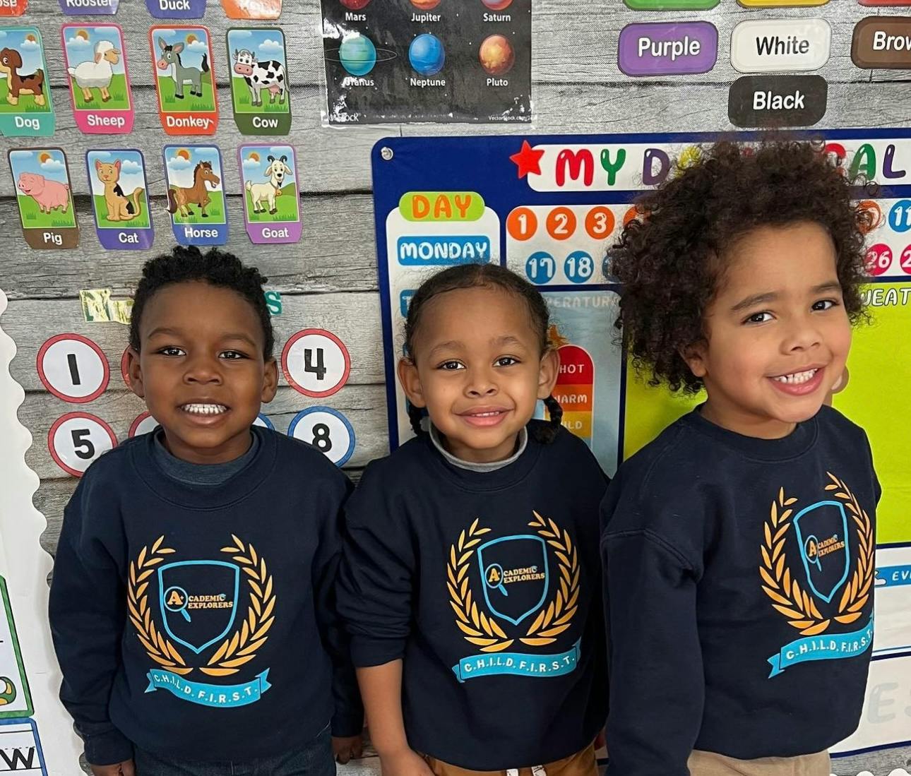 Three children in matching shirts standing in a classroom