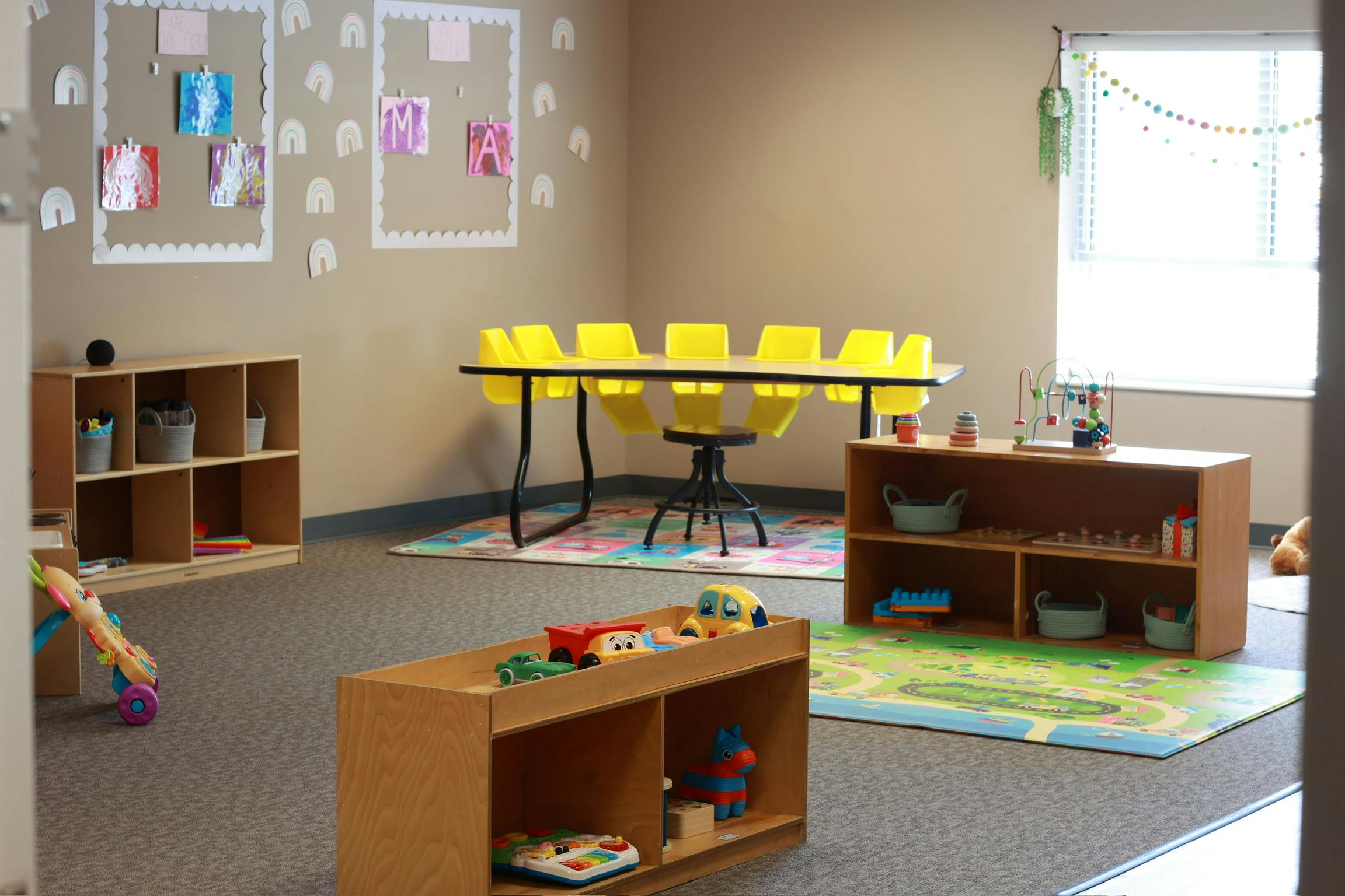 Empty classroom with small tables, chairs, and shelves with toys