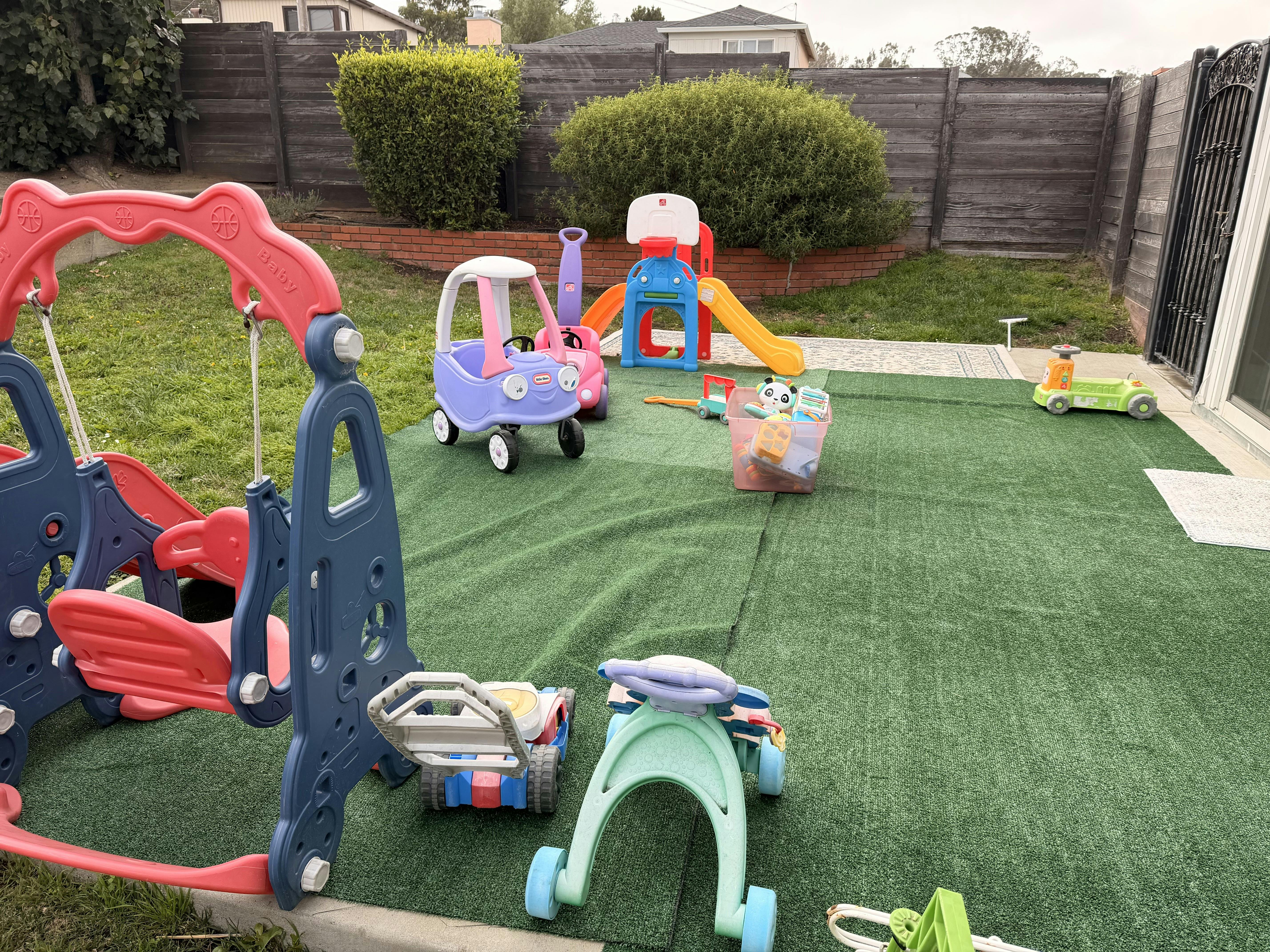 Plastic playground equipment and ride-on toys on a backyard artificial lawn
