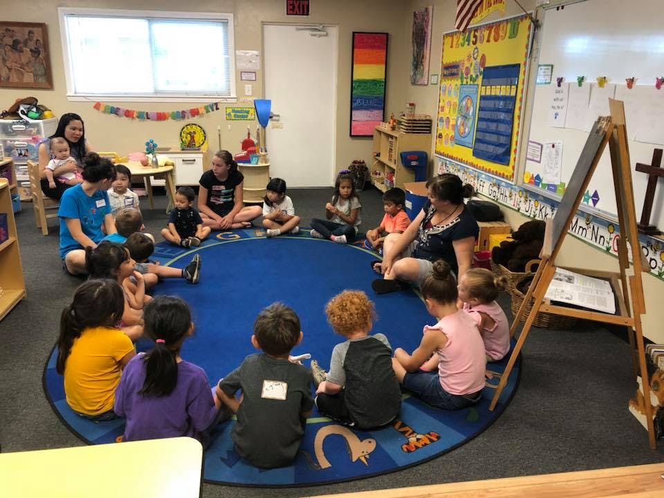 Adults and children sitting in a circle on a blue rug in a classroom