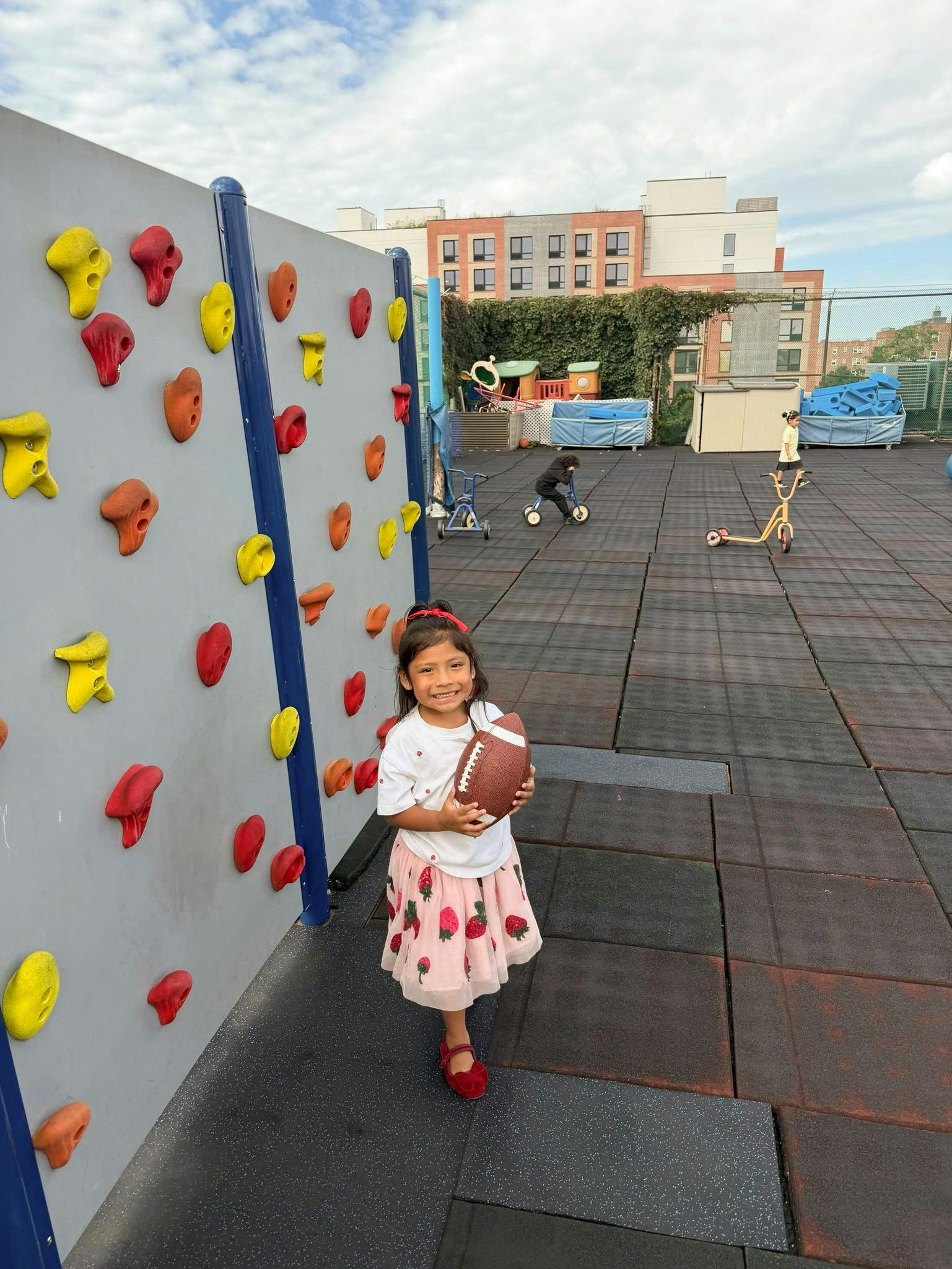 Child holding a football on a playground near a climbing wall