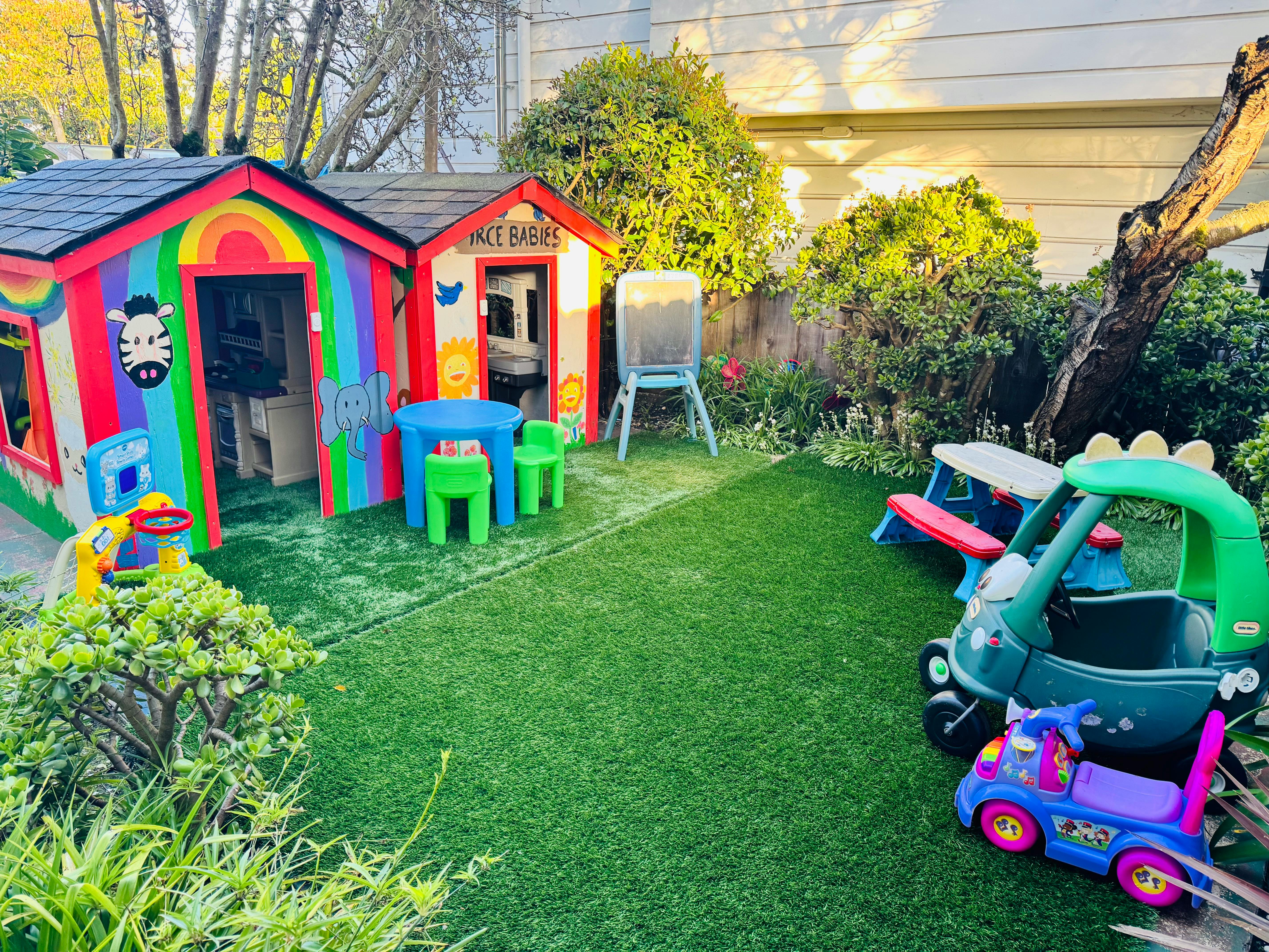 Backyard with two colorful playhouses, a blue table with green chairs, and toy cars