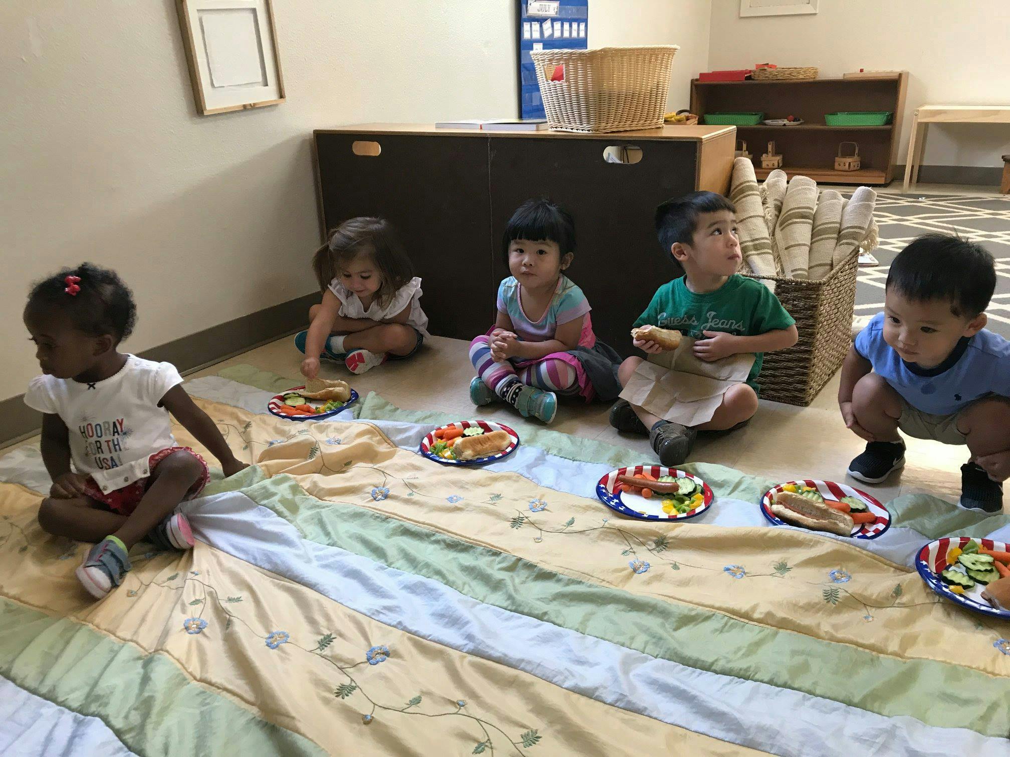 Five children sitting on a blanket with plates of food