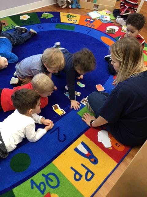 Adult and multiple children on a colorful alphabet rug in a classroom