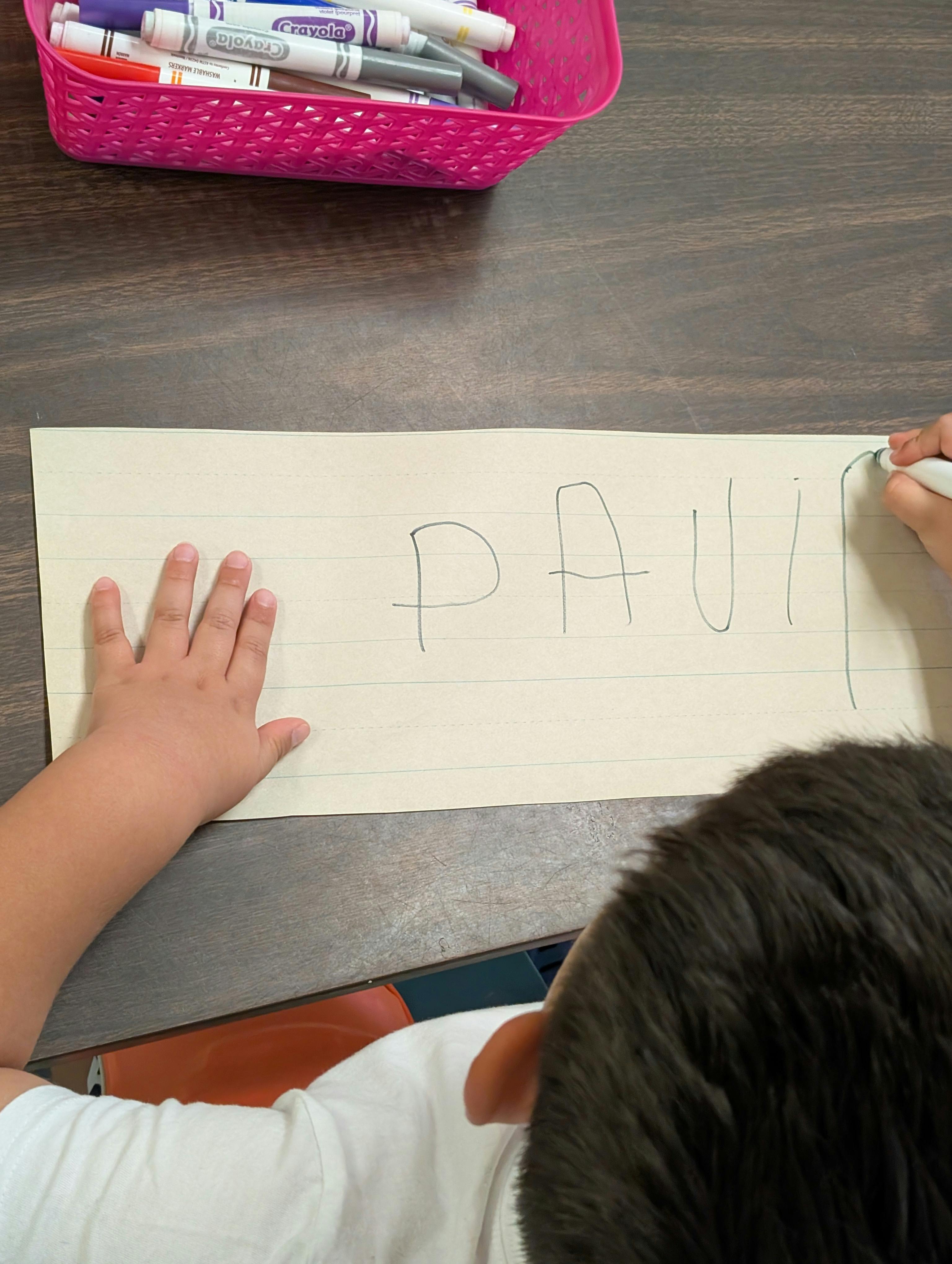 Child writing the letters PAUI on lined paper