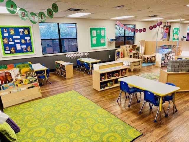Empty classroom with small tables and chairs, shelves, and a green rug
