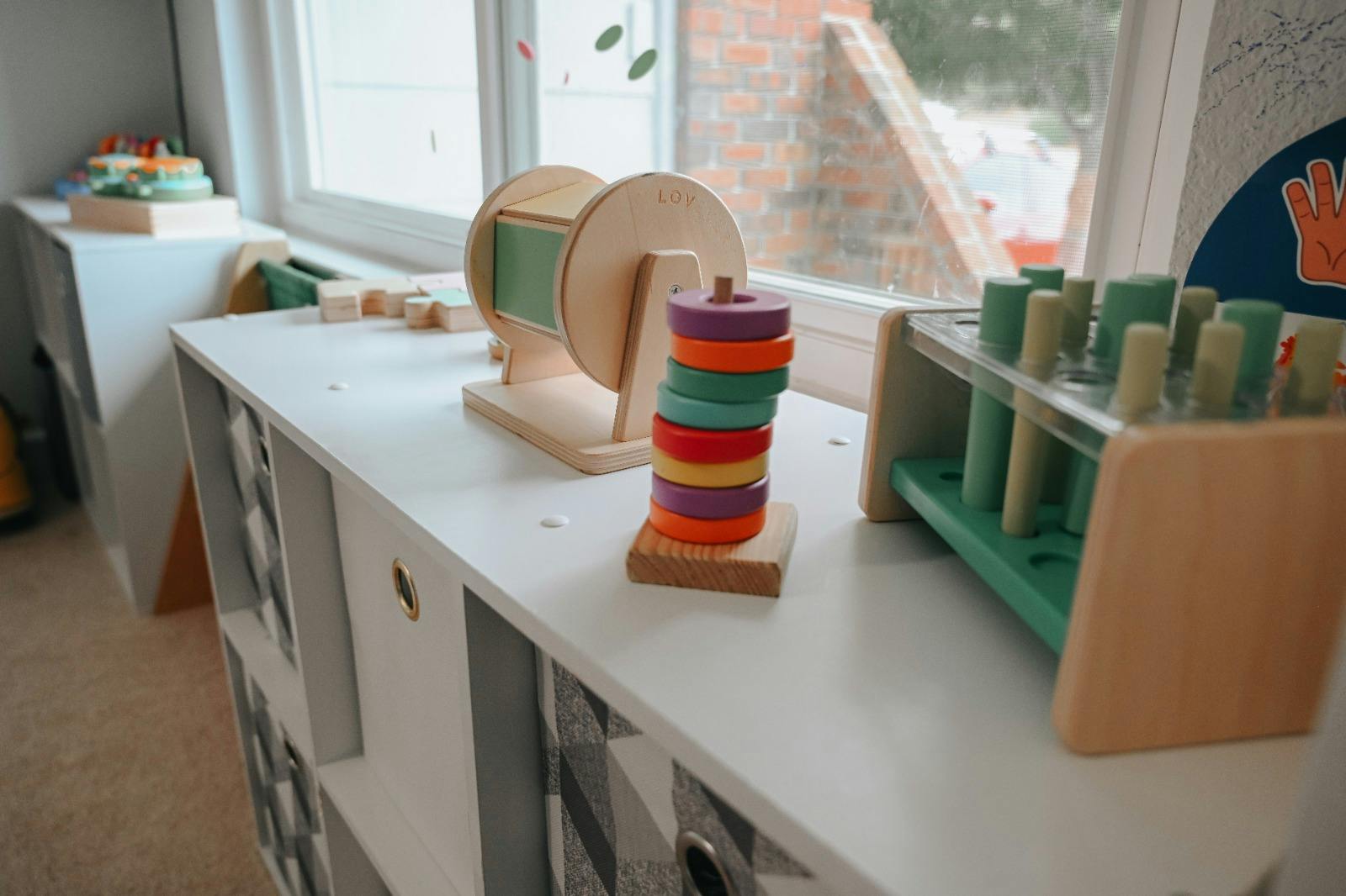Wooden toys on a white shelf, including a ring stacker and a test tube rack