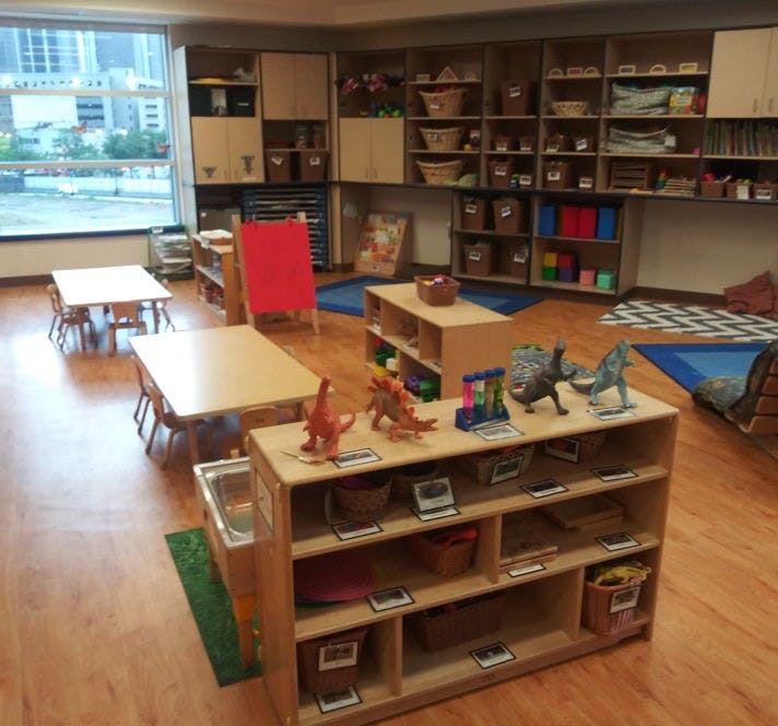 Classroom with small tables and chairs, shelves with toys and learning materials