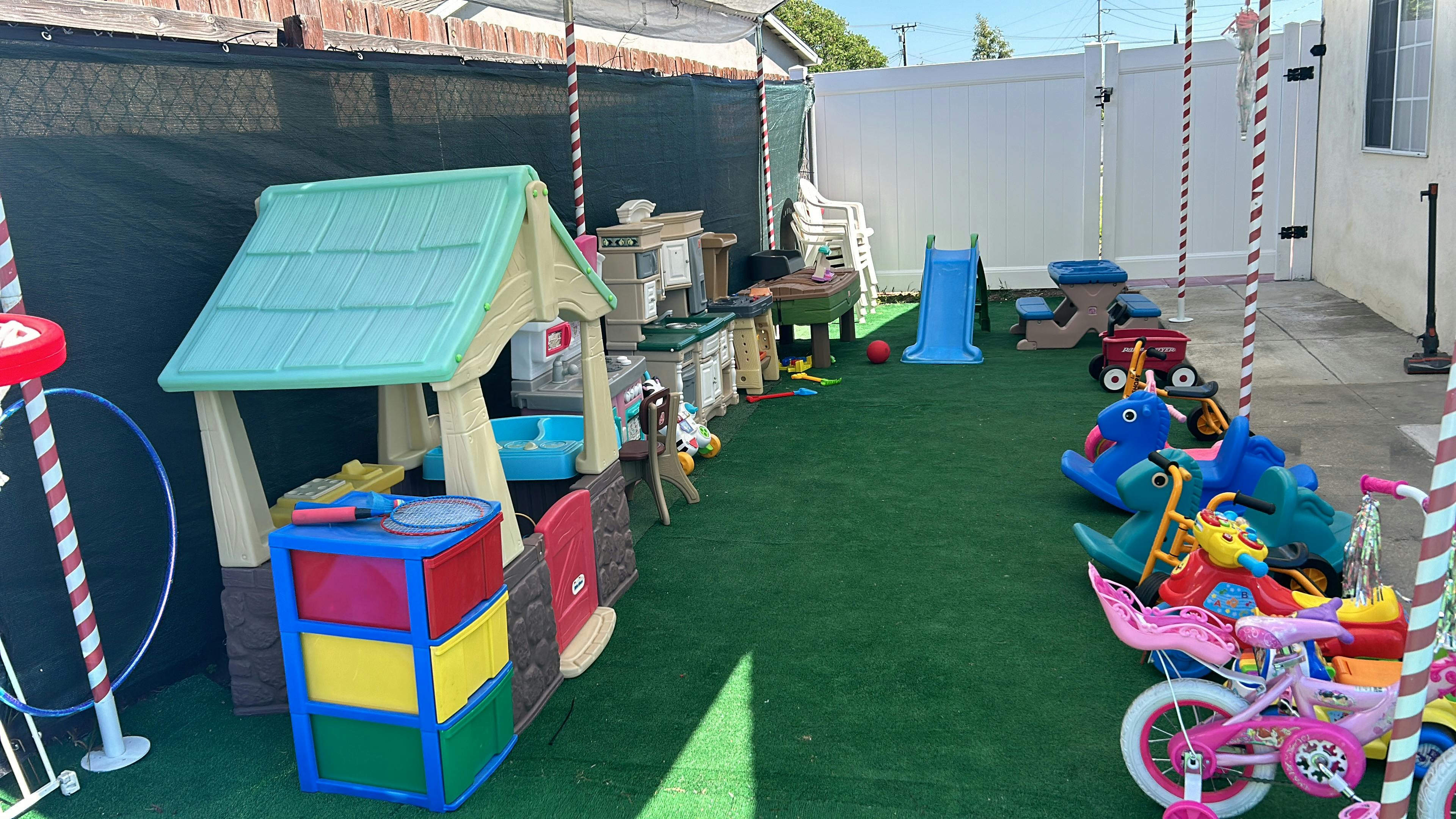 Outdoor play area with various toys including a playhouse, slide, and ride-ons